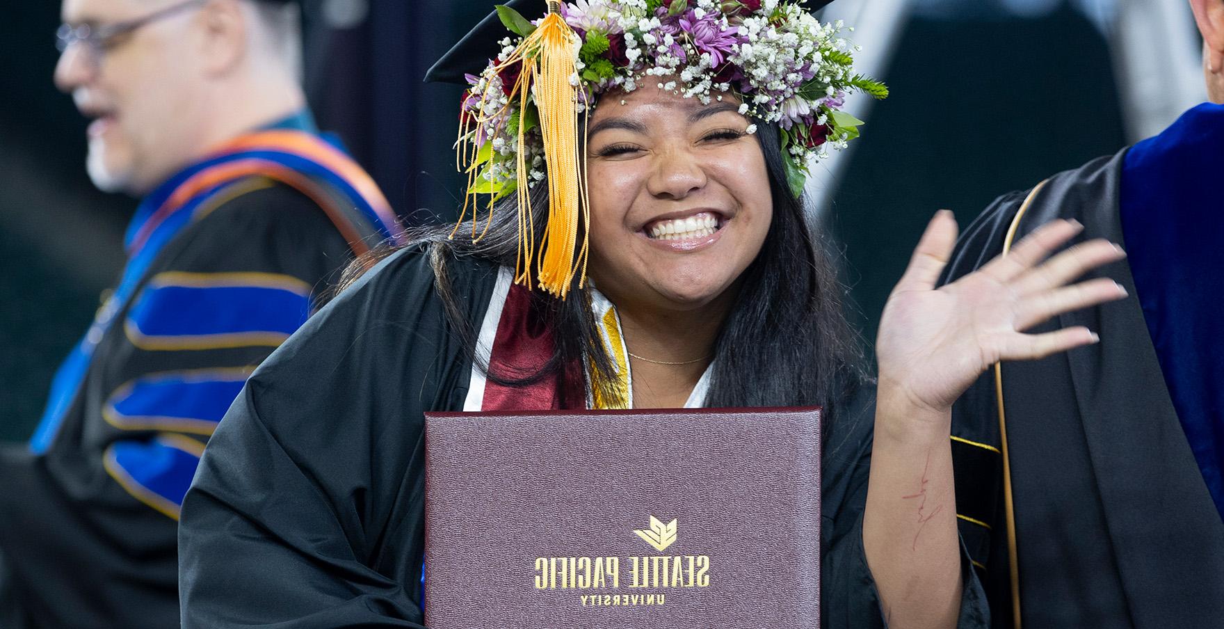 一名西雅图州立大学的学生拿着她的文凭微笑着挥手